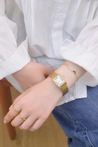 Close-up of a rectangular gold watch with roman numerals on a model's wrist with jewelry