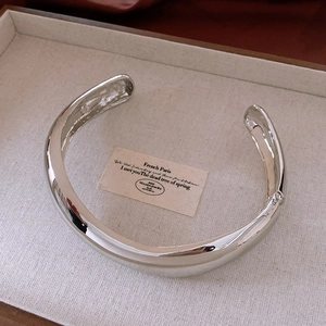 Vue détaillée d'un large bracelet argenté avec finition miroir polie sur un plateau beige