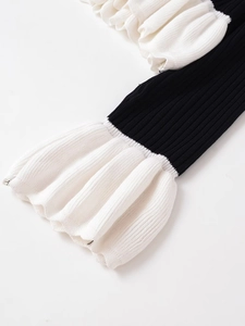 Detail of black ribbed knit sleeve with multi-layered white ruffle flared cuffs