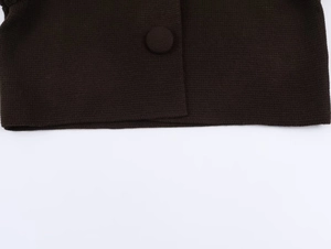 Gros plan d'un gilet en tricot marron foncé avec coutures détaillées et bouton recouvert