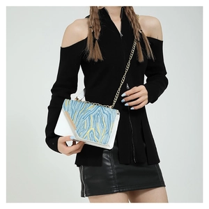 Chic white crossbody bag with blue wave embroidery and golden chain strap shown on model