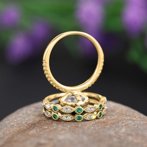Close-up of gold rings with emerald green stones and diamonds on natural stone