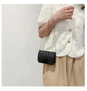Close-up of black quilted mini bag featuring heart buckle and gold chain strap