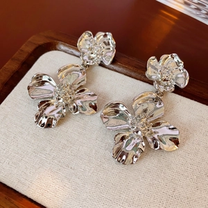 Silver flower earrings with textured petals and zircon centers on a beige linen display