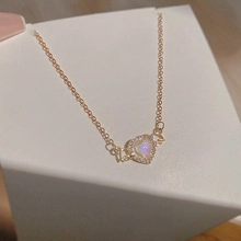 Macro detail of a golden heart necklace with an iridescent white stone and zircon pavé