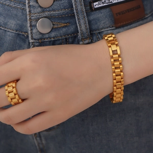 Golden watchband chain bracelet and matching ring set worn on hand over denim background