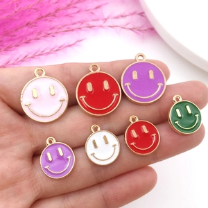 Handheld assortment of colorful enamel smiley face pendants with gold trim for DIY jewelry