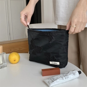 Minimalist black makeup pouch with embroidered bow and vivid blue lining held by hands