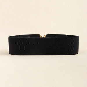 Close-up of black elastic belt featuring a polished gold C-shaped metal interlocking buckle