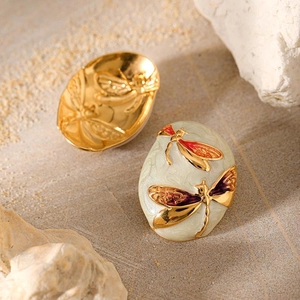 Macro shot of oval gold-plated earrings with enamel dragonfly and embossed metallic details