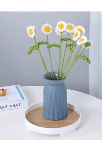 Handcrafted crochet white daisies with yellow centers in a blue ceramic vase on a white tray