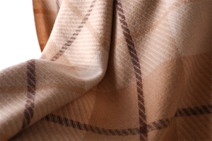 Close-up of soft beige and brown plaid cashmere-feel fabric texture and tassel details