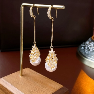 Détail de boucles d'oreilles dorées à glands avec zircons et perles blanches élégantes
