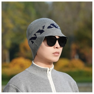 Close-up of a grey ribbed knit beanie with blue letter detail worn in an outdoor setting
