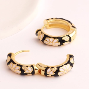 Detail of golden hoop earrings with black enamel and white daisy floral patterns