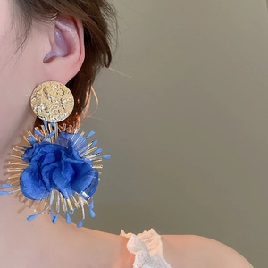 Close-up of bohemian style earrings with blue fabric flowers and golden metal accents