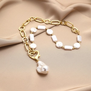 Detailed view of baroque pearl necklace with gold chain on champagne silk fabric