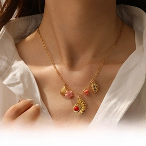 Close-up of a gold conch and starfish charm necklace with a red stone on a white shirt