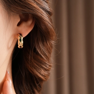 Close-up of vintage golden C-shaped earrings with red and green enamel diamond patterns
