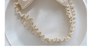 Macro shot of beige lace baby headband with sparkling bow detail on a ceramic plate