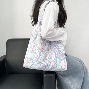 Side view of large canvas tote bag with dynamic blue and red wavy patterns on model