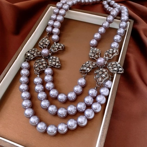 Detail of multi-layer purple pearl necklace with floral crystal pendants on brown silk