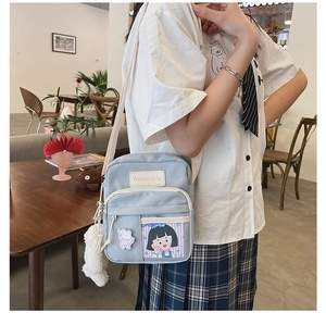 Détail du sac bandoulière en toile bleu clair avec écusson dessin animé et pendentif