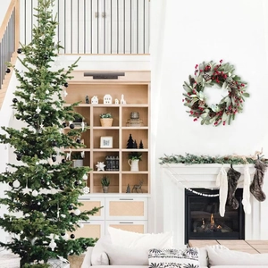 Christmas wreath with pine cones and red berries hanging above a fireplace in a cozy room