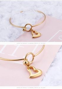 Detail of a minimalist gold open bangle featuring a 3D hollow heart pendant and polished finish