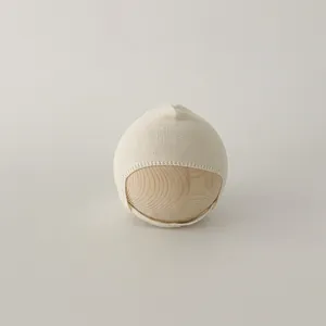 Close-up of cream knit baby bonnet featuring fine stitching and soft chin strap
