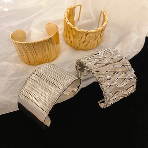 Close-up of gold and silver braided cuff bracelets with industrial brushed metal texture