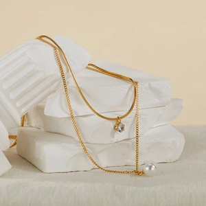 Detailed close-up of double-layer gold snake chain necklace with pearl and zircon pendant