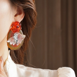 Detail of earring with red rose and white goldfish on model in white shirt