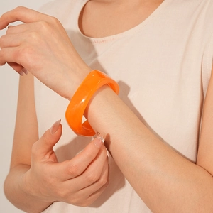 Close-up of a bold orange resin square bracelet worn by a model over white knitwear