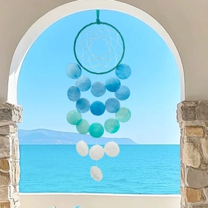 Handmade shell wind chime hanging by a coastal window with blue ocean view background
