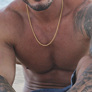 Detailed view of a golden stainless steel keel chain worn by a male model on a beach