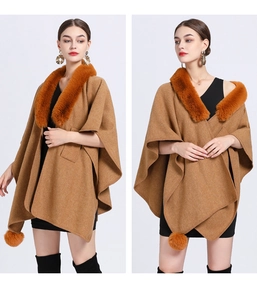 Detail of a brown knitted poncho featuring a bright orange faux fur collar and pom-pom accent