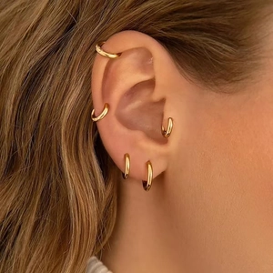 Detailed view of five polished gold hoop earrings worn together on a model's ear cartilage
