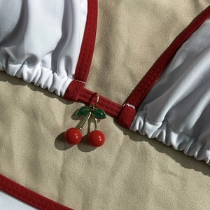 Detail of red cherry charm on tricolor mesh bikini top with white pleated texture