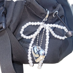 Chic white faux pearl bow bag charm featuring a polished silver heart pendant on a black bag