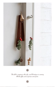 Vintage brass Christmas bell hanging on a white door with pine needles and red berries