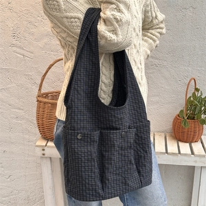 Detail of grid canvas tote bag with front pockets and broad shoulder strap on a model