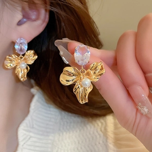 Close-up of elegant gold flower earrings with a purple gemstone and pearl detail