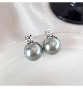 Macro shot of grey pearl earrings with cubic zirconia inlay on white porcelain surface
