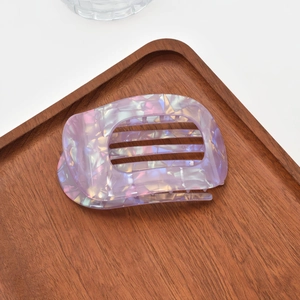 Macro detail of lavender iridescent acetate hair claw clip on a dark wood tray