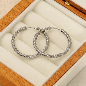 Elegant silver twisted rope hoop earrings displayed on a white velvet jewelry box base