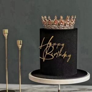 Macro view of golden Happy Birthday topper and crown on a black tiered cake
