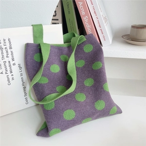 Dettaglio di borsa tote in maglia viola a pois verdi su uno scaffale bianco sobrio