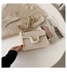 Straw crossbody bag with pearl chain detail styled on a white table with newspapers