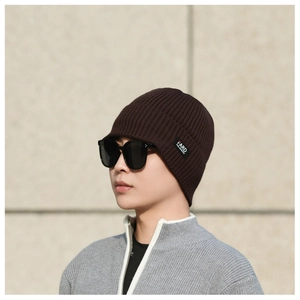 Detail of dark brown ribbed knit beanie with small black brand label on a model